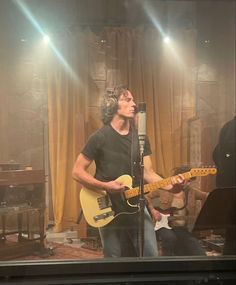 a man standing in front of a microphone while holding a guitar