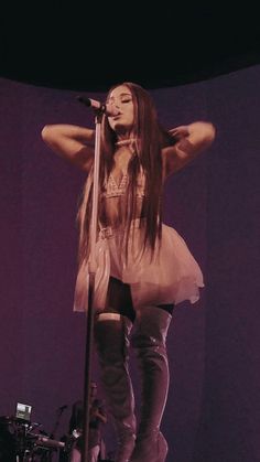 a woman standing on top of a stage with her arms behind her head and holding a microphone