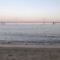 a bridge spanning the width of a large body of water next to a sandy beach