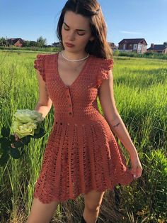 a woman in an orange crochet dress holding a flower