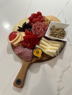 a wooden paddle with cheese, meats and fruit on it sitting on a marble counter top