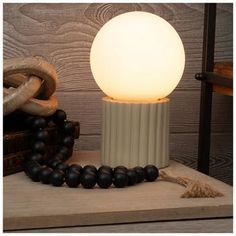 a white lamp sitting on top of a wooden table next to a black bead necklace