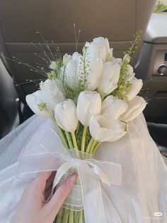 a bouquet of white tulips tied to a ribbon in a vase on the back seat of a car