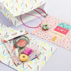 two gift bags with different items in them on a white surface and colorful confetti