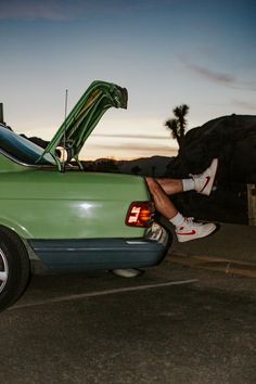 a man sitting on the back of a green car with his feet in the trunk