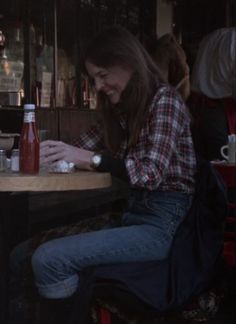 a woman sitting at a table with a soda bottle in her hand and another person standing next to her