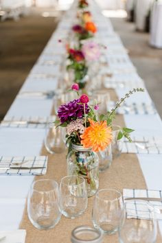 a long table with vases filled with flowers and glasses on top of each one