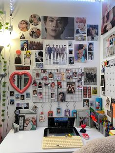 a laptop computer sitting on top of a desk next to a wall covered in pictures