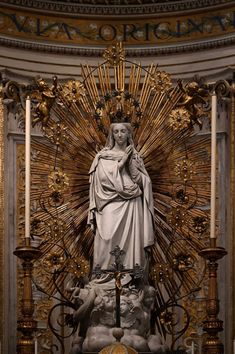 a statue of the virgin mary in front of a golden alter with candles on it