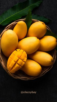 a basket filled with lots of yellow fruit next to green leaves on top of a table