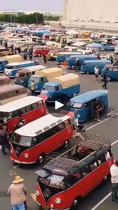 a parking lot filled with lots of different colored buses and people standing around them in front of buildings