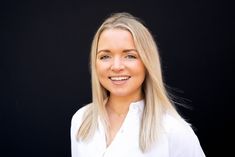 a woman with blonde hair smiling at the camera and wearing a white shirt against a black background