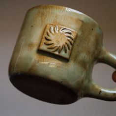 a hand holding a ceramic cup with a sun design on it