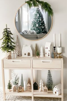 a christmas scene with miniature houses and trees on a shelf in front of a mirror