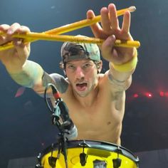 a shirtless man holding up two sticks above his head while standing in front of a drum set