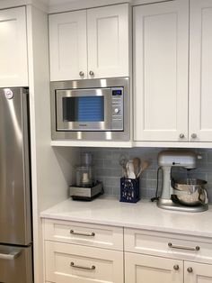 a kitchen with white cabinets and stainless steel appliances, including a microwave on the wall