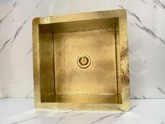 a gold square shaped sink sitting on top of a white counter next to a marble wall