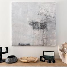 an abstract painting hangs on the wall above a shelf with other items and sculptures in front of it