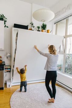 a woman standing next to a child in front of a large white board on the floor