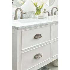 a white bathroom vanity with two sinks and mirrors on the wall above it is also a vase with flowers