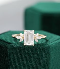 an emerald colored ring with leaves on the side and a diamond in the middle, sitting on top of a green velvet box