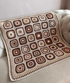 a crocheted blanket sitting on top of a couch next to a white chair