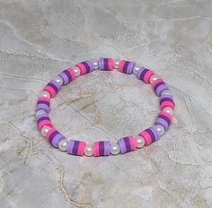 a pink and purple beaded bracelet sitting on top of a stone surface with beads