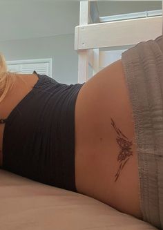 a woman laying on top of a bed with a tattoo on her lower back and arm