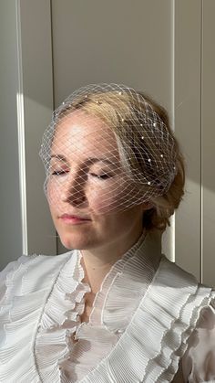 a woman in a white dress with a birdcage veil on her head, looking off to the side