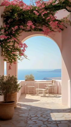 an archway with pink flowers and chairs on the outside, overlooking the water in the background