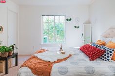 a bedroom with white walls and lots of pillows on the bed, along with potted plants