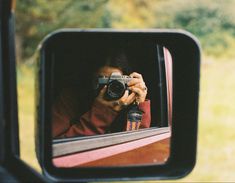 a woman taking a photo in the rear view mirror of a car with her camera