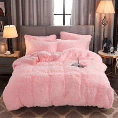 a bed with pink comforter and pillows in a room next to a lamp on a table