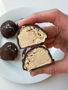 three pieces of chocolate covered ice cream on a white plate with two hands holding it