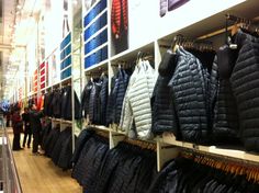 there are many jackets on the shelves in this clothing store and people are looking at them