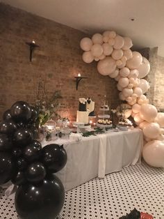 a table with black and white balloons, cake and desserts on it in front of a brick wall