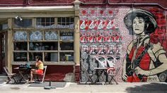 a woman sitting on a chair in front of a building with a mural behind her