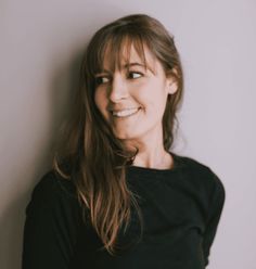 a woman with long brown hair and black shirt smiling at the camera while leaning against a wall