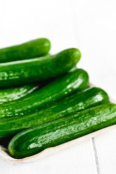 green cucumbers in a white dish on a white tablecloth and wooden boards