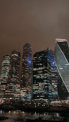 the city skyline is lit up at night with skyscrapers in the foreground and water below