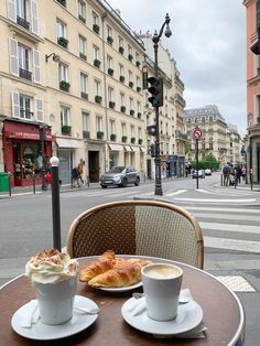 two cups of coffee and croissants sit on a table in front of a street corner