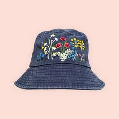 a blue bucket hat with colorful flowers on the front and side, against a pink background