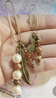 a pair of earrings with pearls and leaves hanging from it's ear hooks on a book page