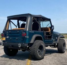 a blue jeep parked in a parking lot next to an open field with no grass