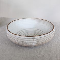 a white bowl sitting on top of a table next to a gray cloth covered floor