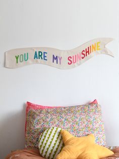 a bed topped with pillows next to a wall mounted sign that says you are my sunshine