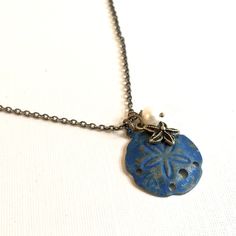 Sand Dollar Necklace - Blue Patina Sand Dollar accented with a an Antiqued Brass Plated Starfish and White Freshwater Pearl. The Sand Dollar is approximately 28mm (slightly larger than an US quarter) and has a hollow back. Antiqued Brass Chain This is a stock photo. There may be slight patina variations. See my Verdigris Collection for similar items. http://www.etsy.com/shop/mcstoneworks?section_id=6573408 Silver Dragonfly Necklace, Star Sand, Sand Dollar Necklace, Dragonfly Jewelry, Jewelry Beach, Starfish Necklace, Ocean Jewelry, Beach Gifts, Bird Necklace