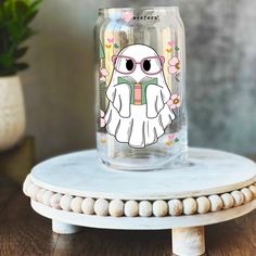 a glass jar with an owl on it sitting on top of a table next to a potted plant