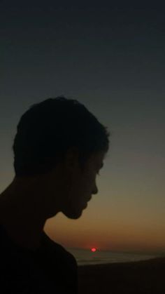 a man standing in front of the ocean at sunset with his head turned to the side