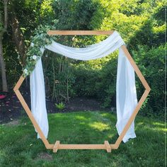 a wooden frame with white draping and greenery on the top is sitting in the grass